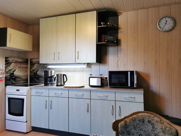 Küche mit Holzverkleidung, Kühlschrank, Herd, Mikrowelle und Uhr an der Wand.