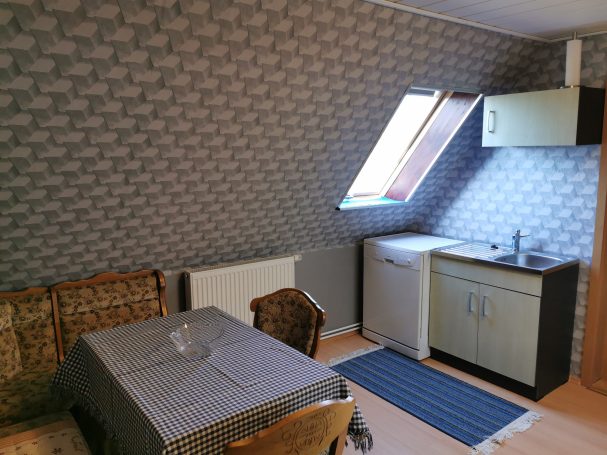 Kleine Küche mit einem Tisch, Stühlen und einem Fenster unter dem Dach.