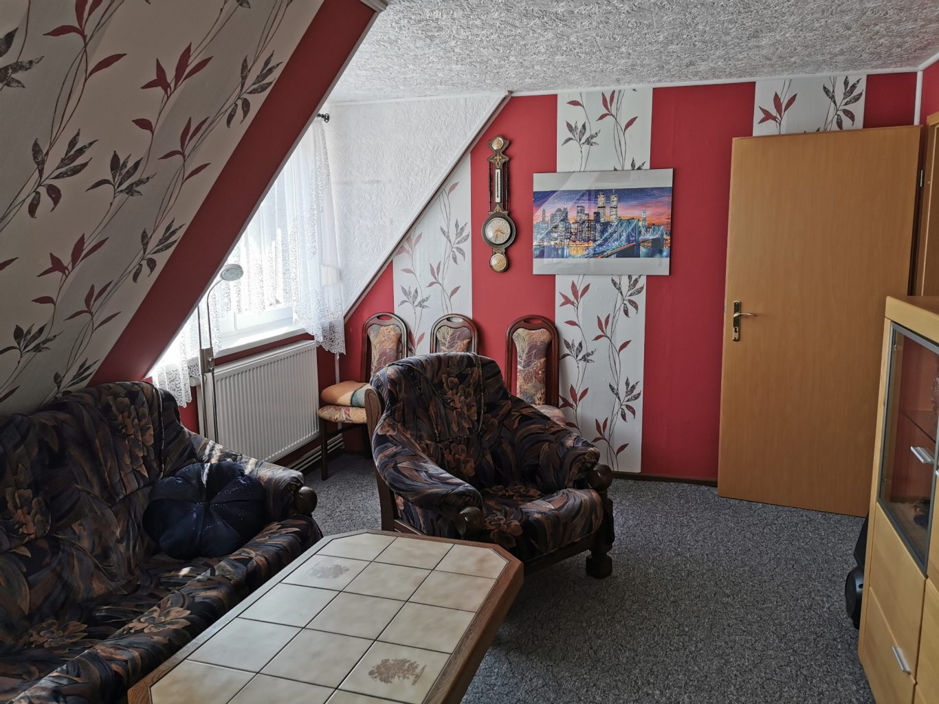 Gemütliches Zimmer mit sofaartigen Sitzmöbeln, Tisch und dekorierten Wänden.