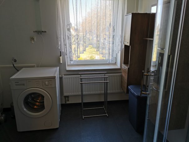 Helle Waschküche mit Waschmaschine, Wäschegestell und einem Fenster mit Ausblick.
