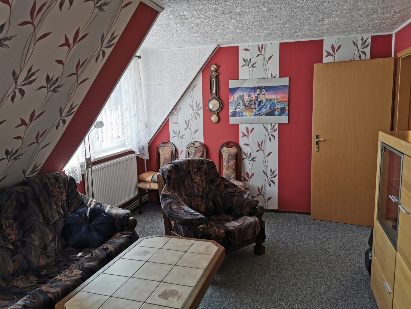 Wohnzimmer mit roter Wand, Sofa, Sesseln und einem Tisch. Kunstwerk an der Wand.