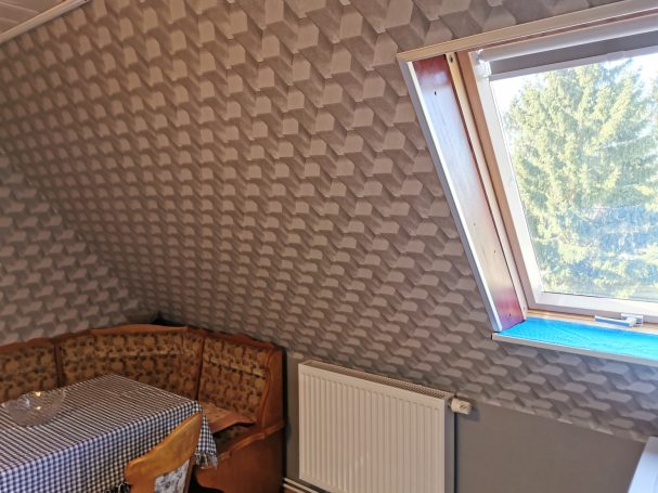 Zimmer mit schräger Wand, Fenstern und Wohnzimmermöbeln.