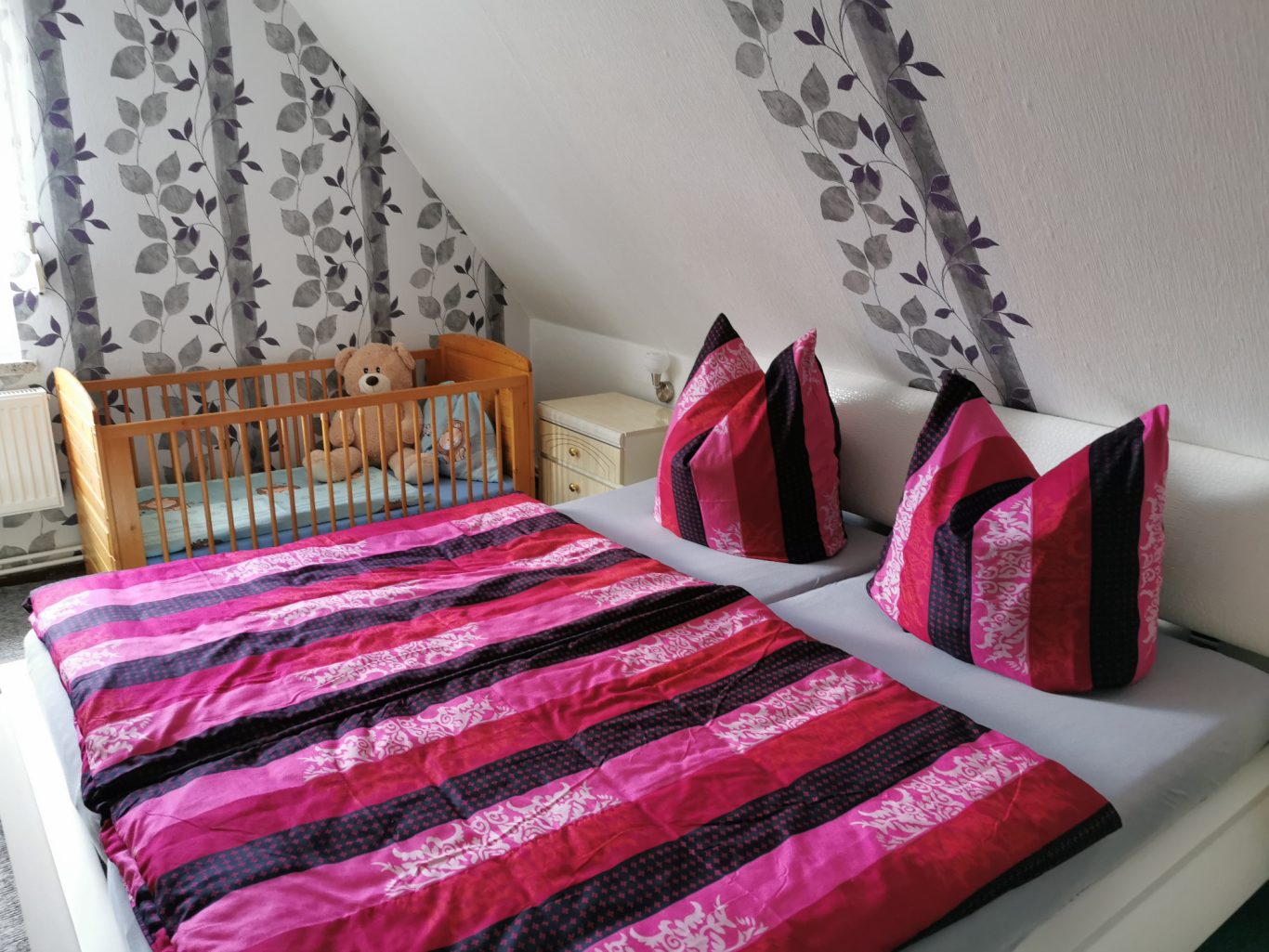 Gemütliches Schlafzimmer mit einem Bett und gestreiften Kissen in Rosa- und Schwarztönen.
