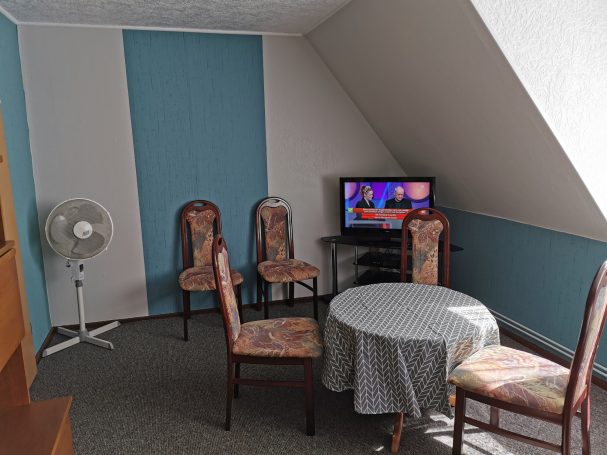 Gemütlicher Zimmer mit Tisch, Stühlen, Ventilator und Fernseher unter einem Schrägdach.