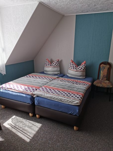 Doppelbett mit gestreiften Matratzen und zwei Kissen in einem Zimmer mit Stuhl.